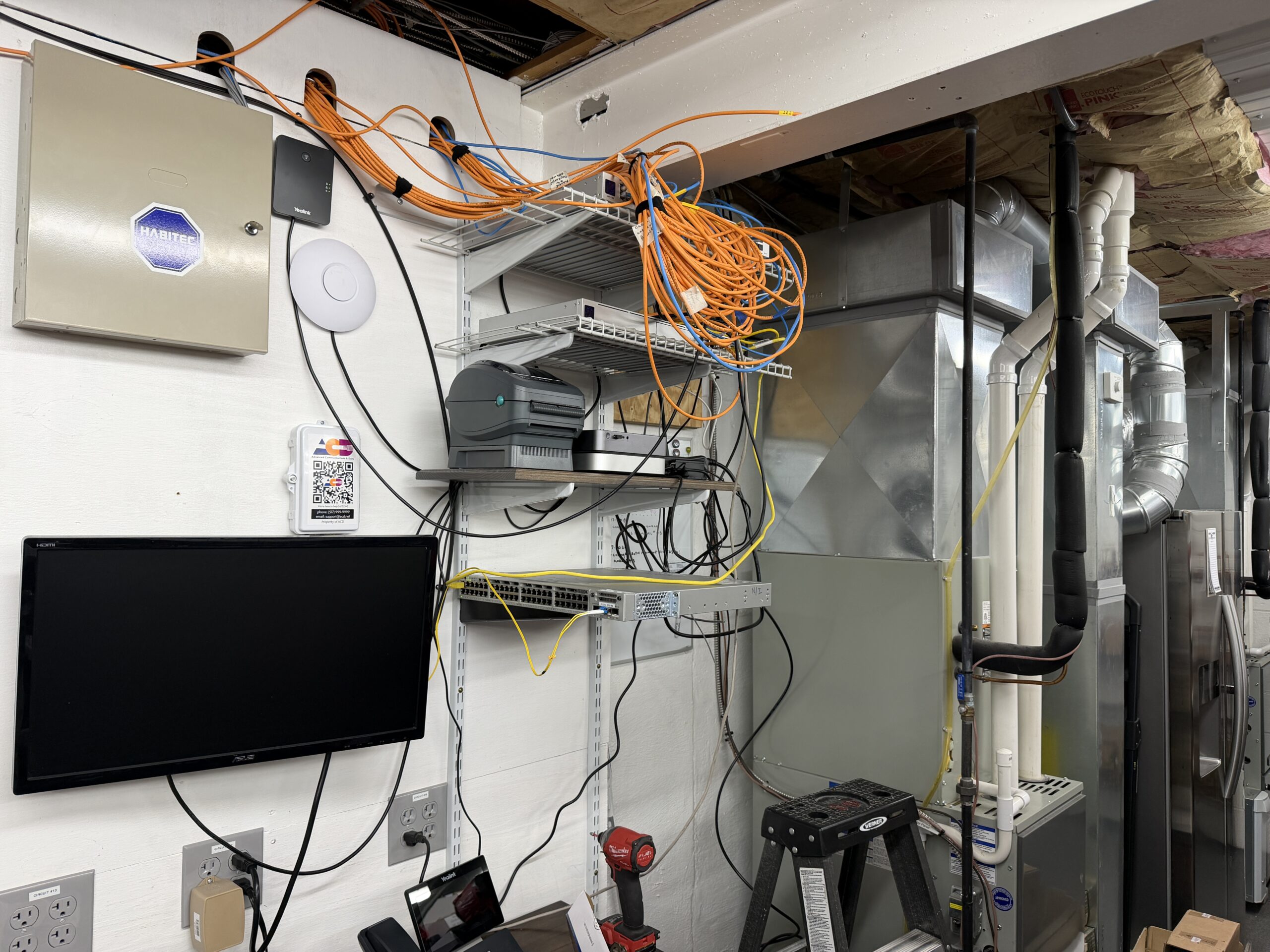 Before — open wire shelving, bundled orange cables piled overhead, no enclosure, cabling running everywhere